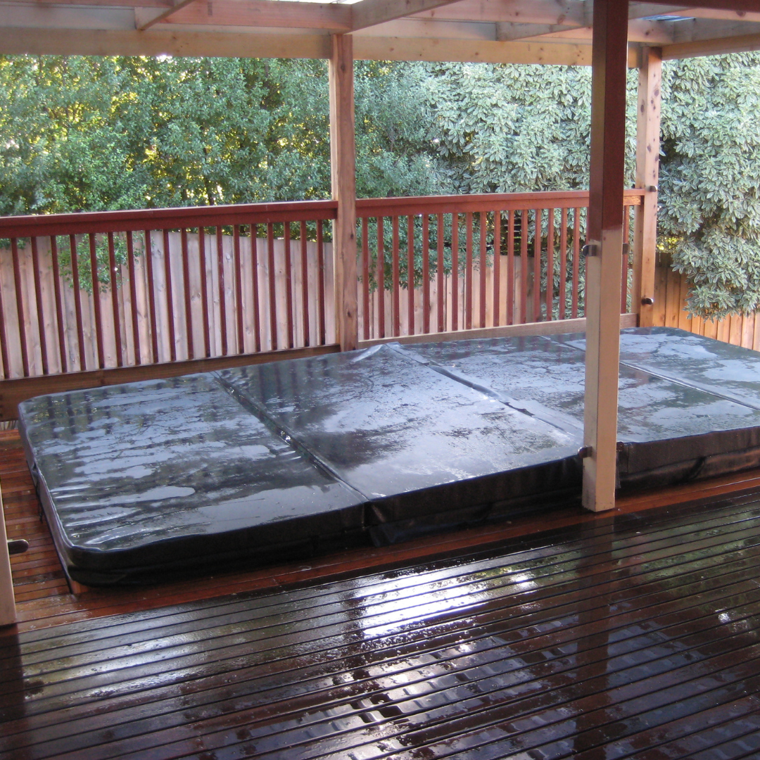 A 4-piece black vinyl hard swim spa cover installed on an outdoor timber deck under a wooden pergola.
