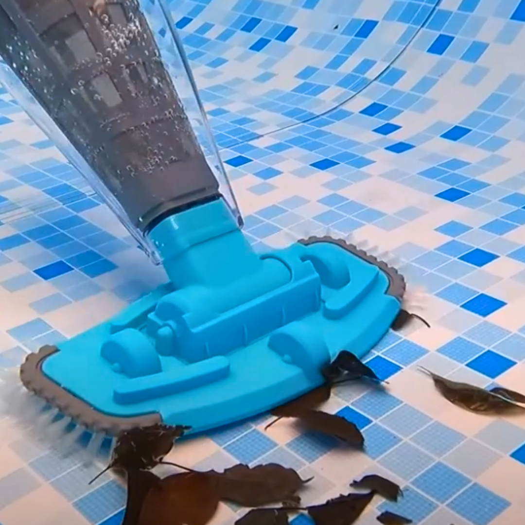 Kokido Telsa 50 handheld pool vacuum head sucking up brown leaves from a blue and white tiled swimming pool floor underwater