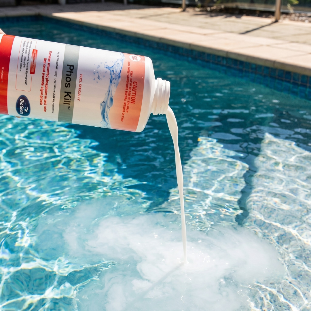 Close-up of a person pouring BioGuard Phos Kill phosphate remover from a 1-liter bottle into a swimming pool, showing the white liquid mixing with the clear blue water to prevent algae growth.