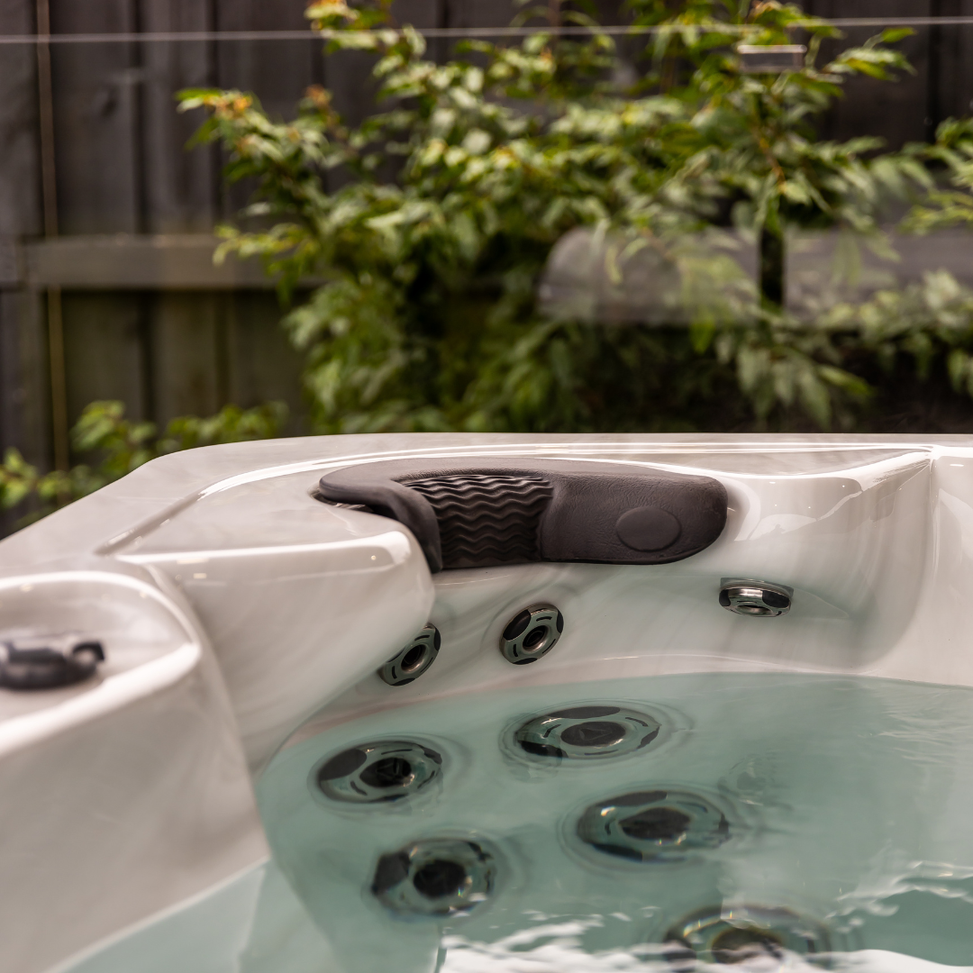 An Artesian Spas Island series neck collar charcoal grey headrest pillow installed in an outdoor backyard hot tub above a hydrotherapy jet cluster.