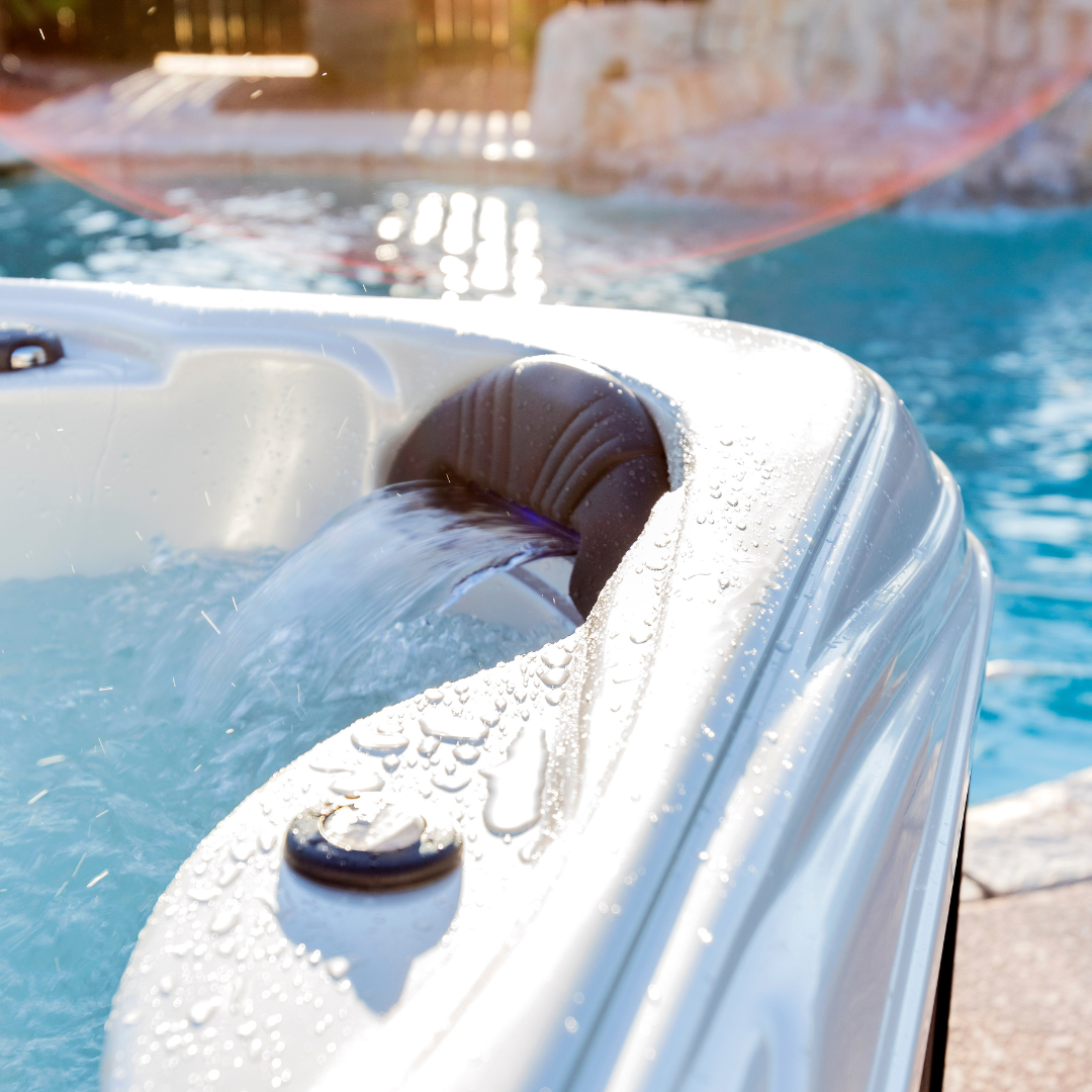 An Artesian Spas Island series charcoal grey waterfall headrest pillow with flowing water, installed in a backyard hot tub adjacent to a swimming pool.