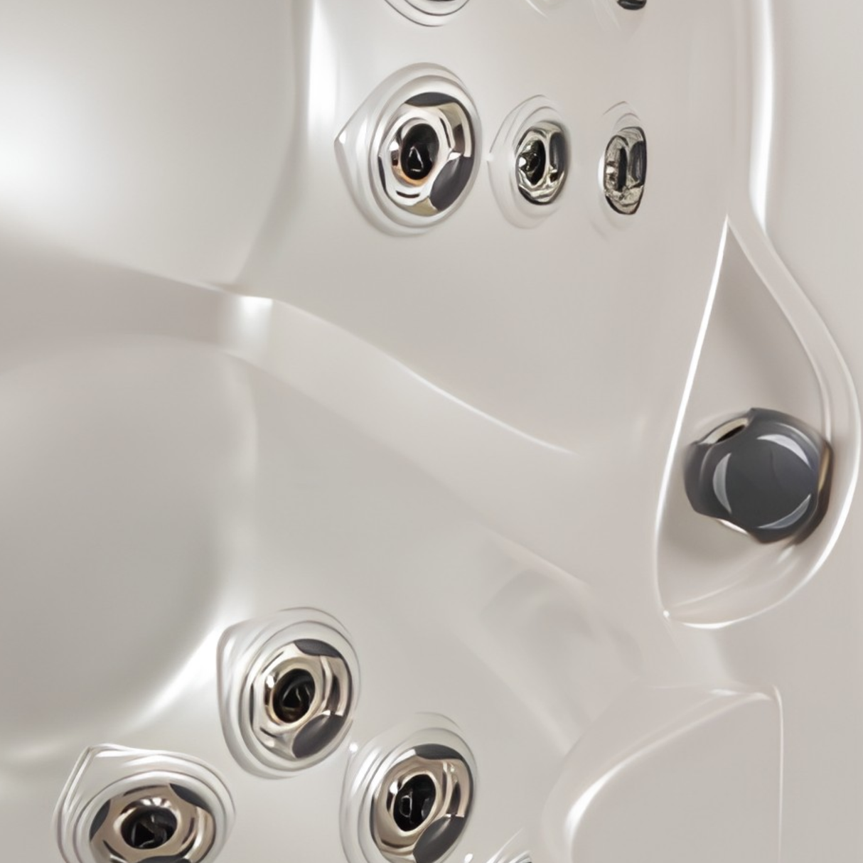 Close-up view of an installed graphite grey Artesian Spas 2-inch diverter valve knob alongside chrome spa hydrotherapy jets inside an acrylic hot tub shell.