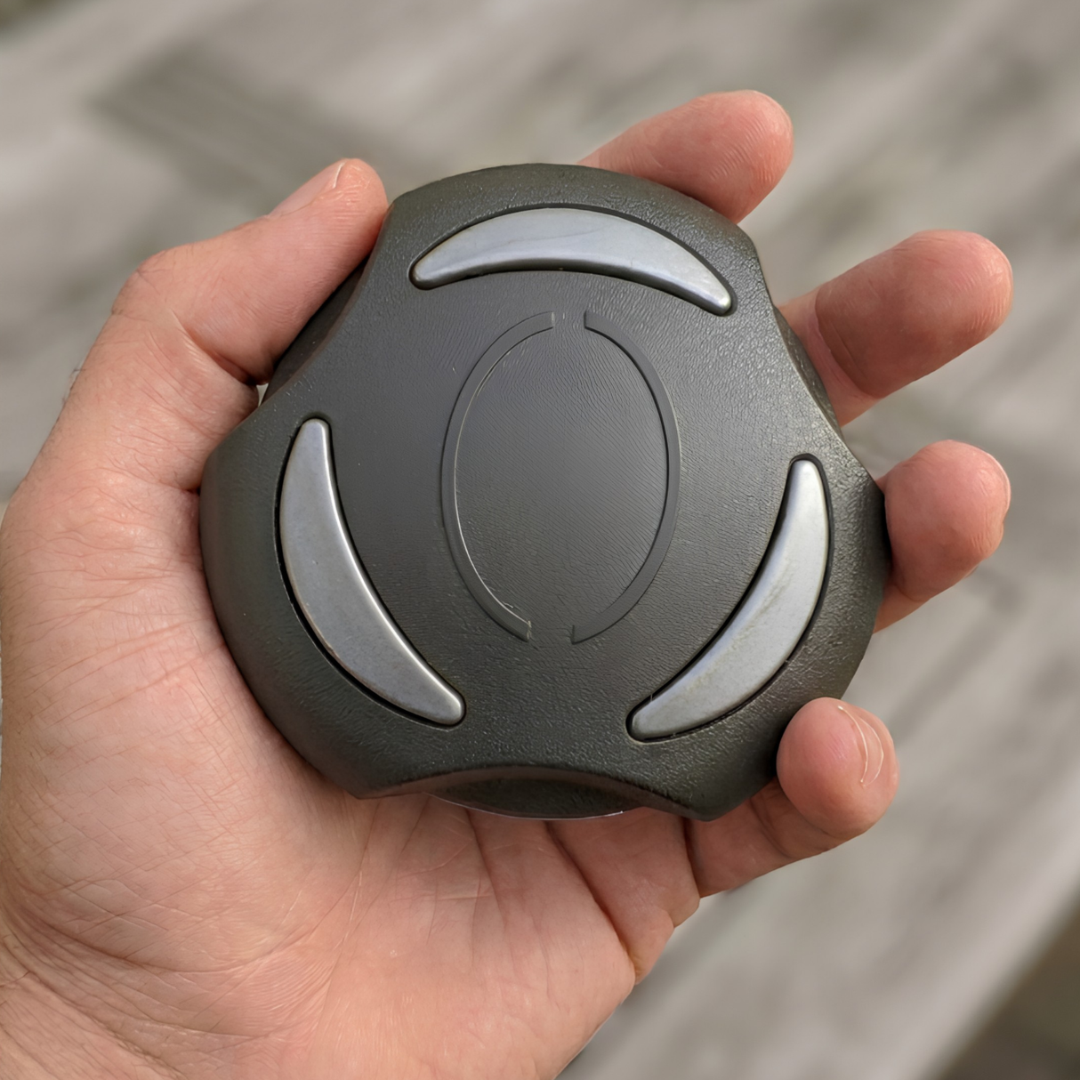 A person holding a graphite gray Artesian Spas 2-inch hot tub diverter valve replacement knob (OP08-1360-52C) in their hand to demonstrate the physical scale and size of the part.