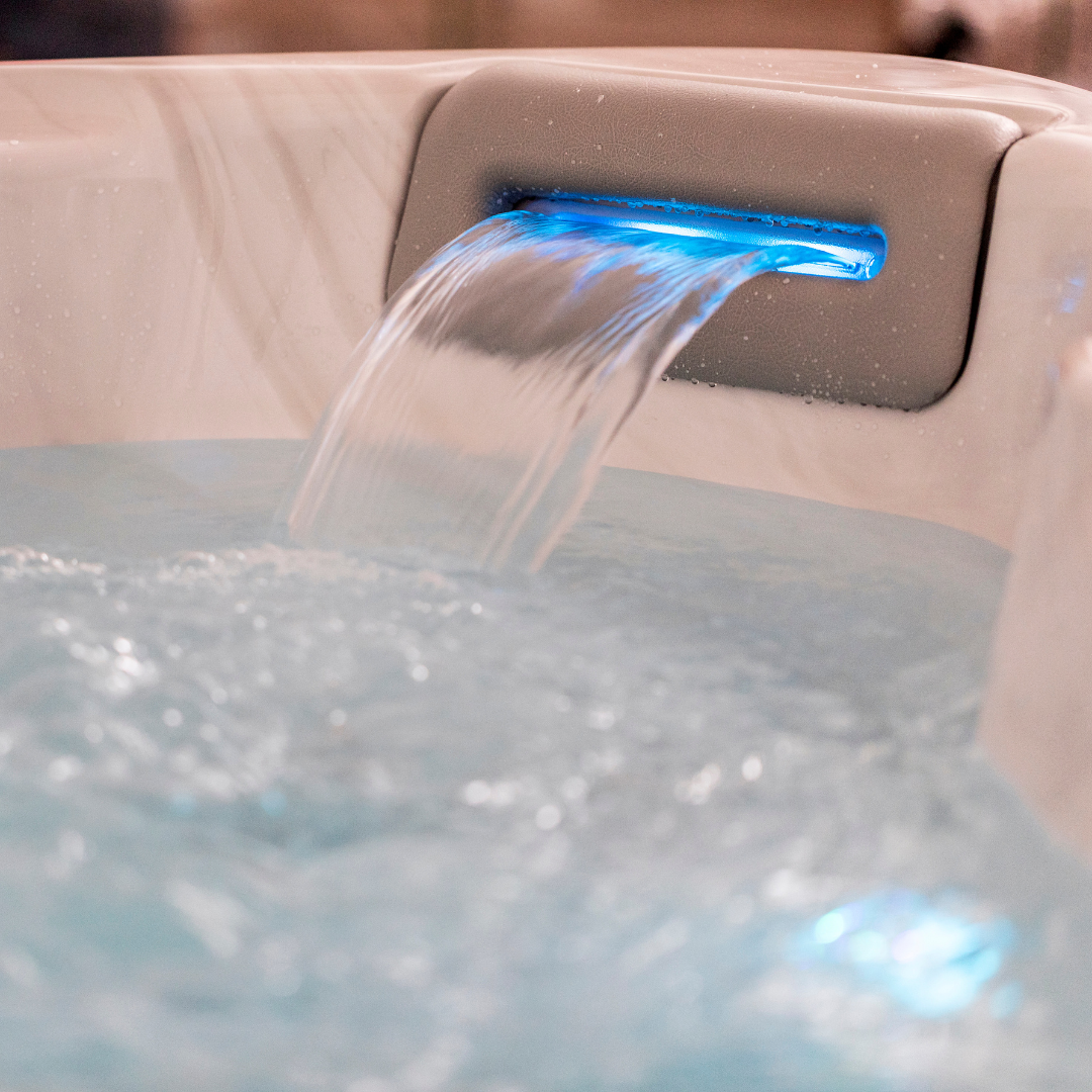Close-up of an Artesian Spas South Seas and Tropic Seas series 8-inch waterfall headrest pillow in light gray, with flowing water illuminated by blue LED lighting inside a hot tub.