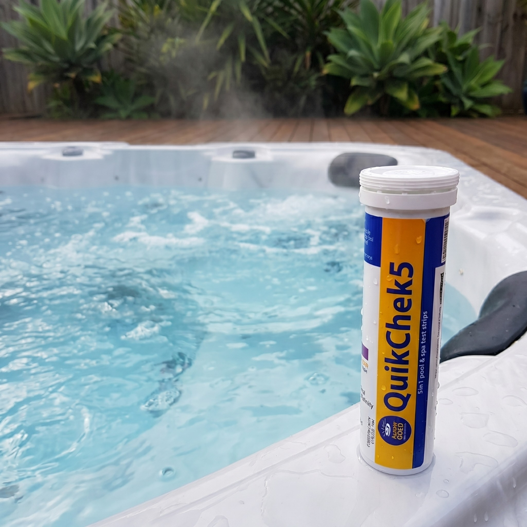A bottle of Aussie Gold QuikChek5 5-in-1 test strips sitting on the edge of a steaming outdoor spa, ideal for monitoring hot tub pH and chlorine levels.