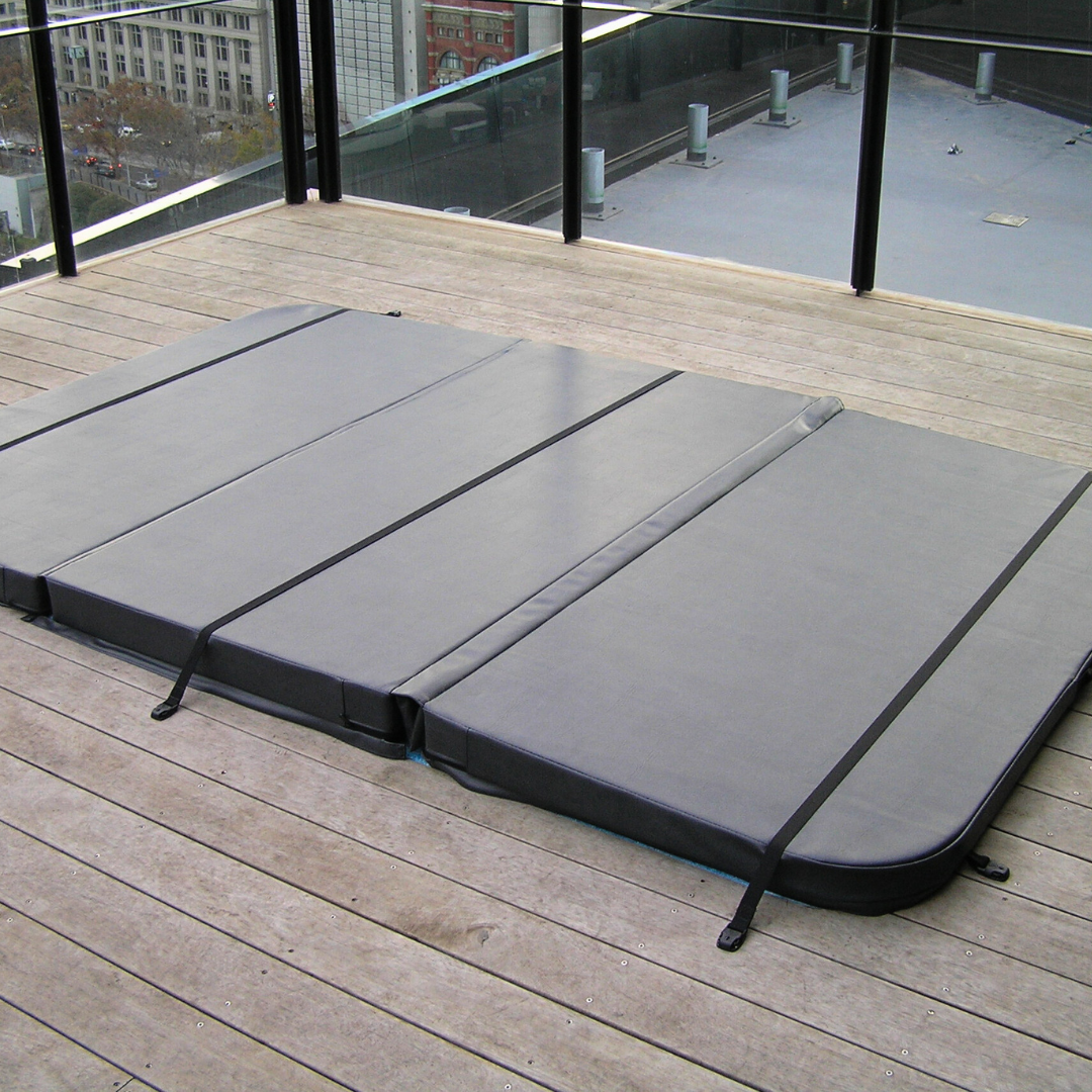 A large custom grey multi-panel swim spa hard cover with safety tie-down straps installed on an outdoor apartment balcony timber deck.