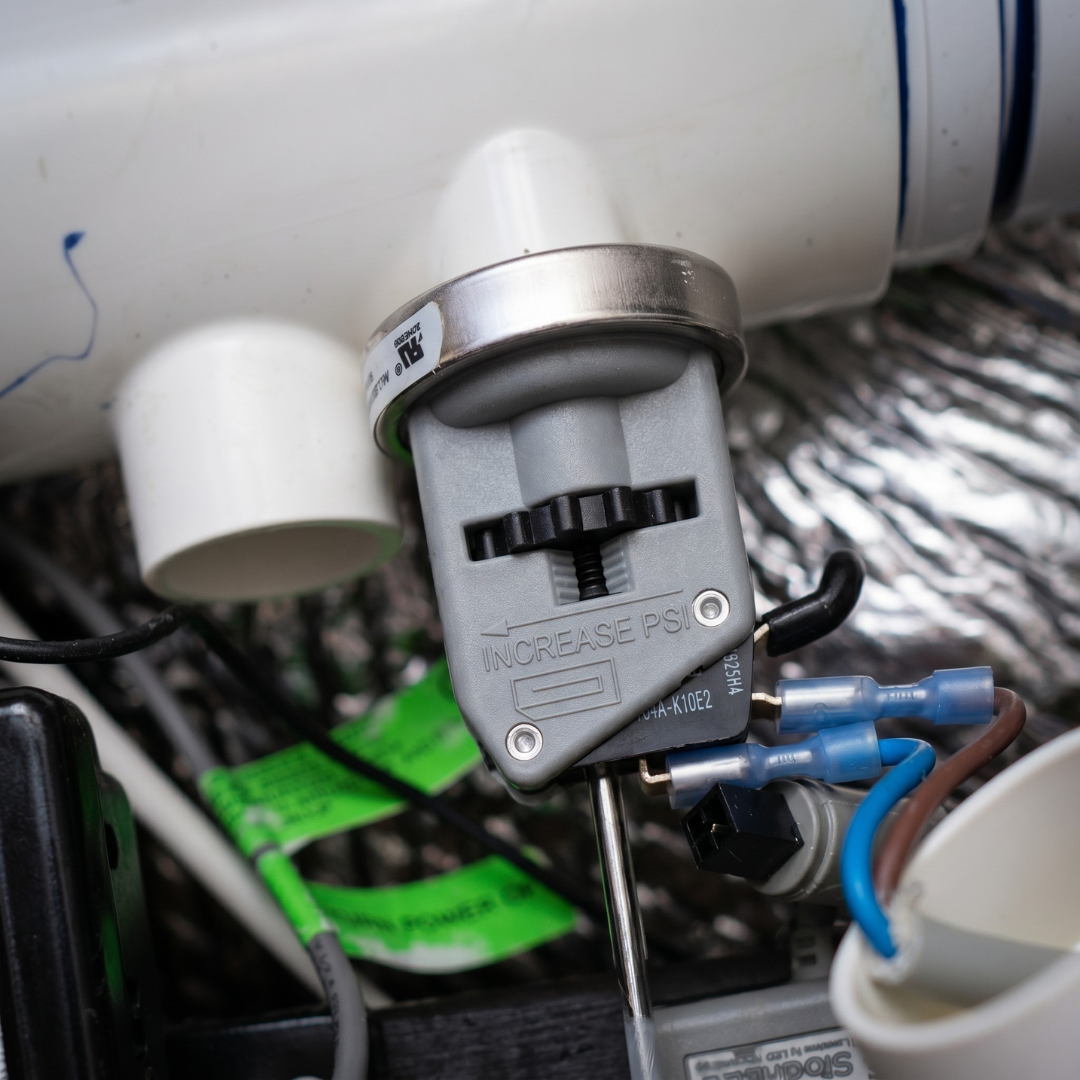 An adjustable pressure switch installed on the plumbing manifold of a Davey Eco Spa salt chlorinator system, showing blue insulated wire terminals connected to the switch terminals.