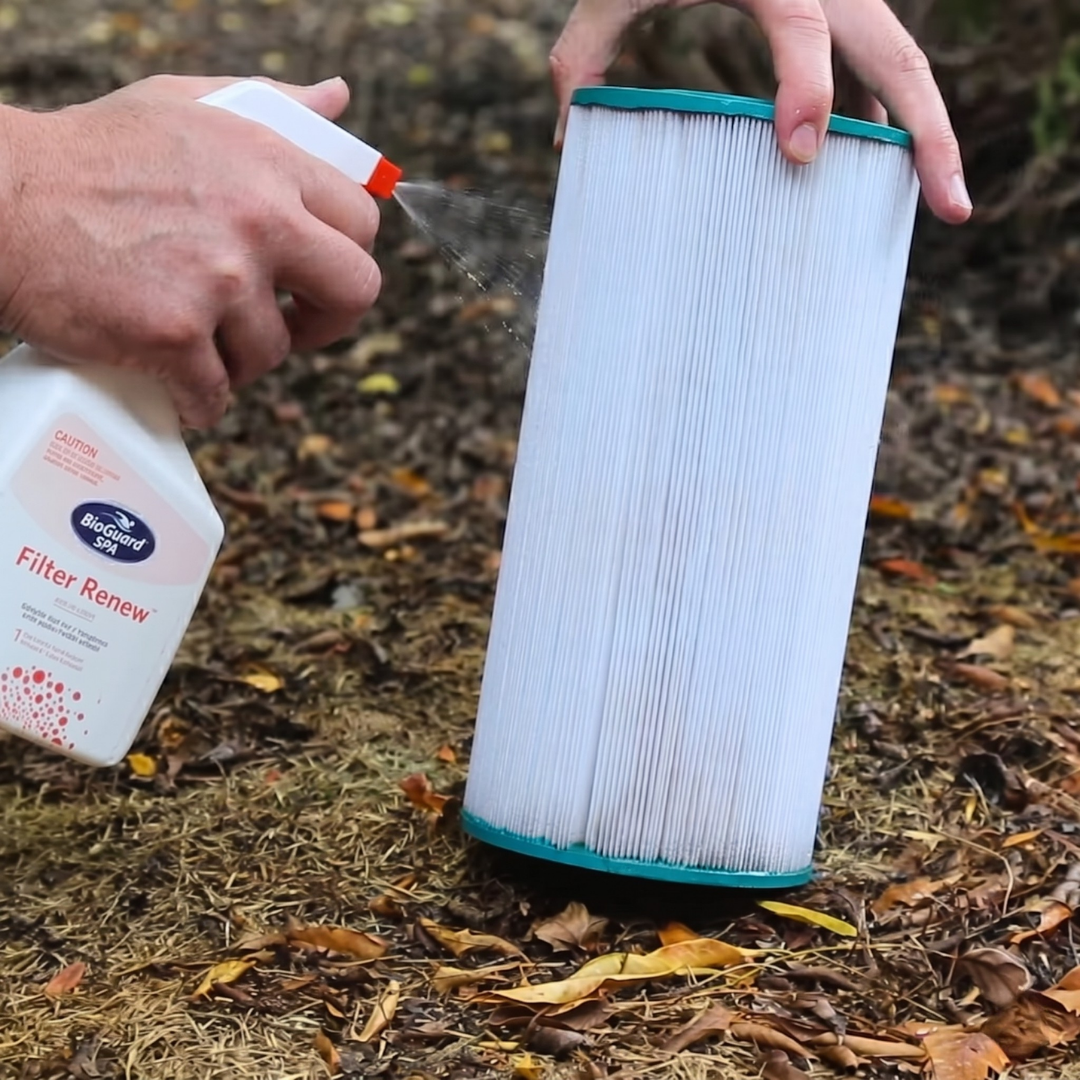 A person spraying BioGuard SPA Filter Renew onto a white pleated spa cartridge filter to remove oils and scale. This spray-on cleaner is an essential part of regular hot tub maintenance and filter deep cleaning.