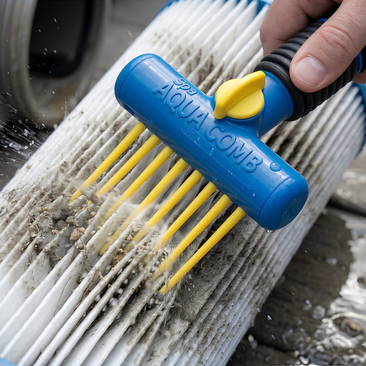 Close-up action shot of a hand using a blue and yellow Spa Aqua Comb tool to spray water and comb out dirt, debris, and grime from a heavily soiled white pleated hot tub cartridge filter