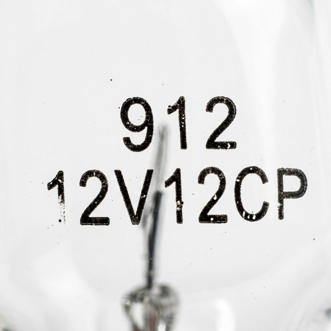 Extreme close-up detail of the black printed specification markings reading 912 12V 12CP on the glass surface of an inground spa light globe.