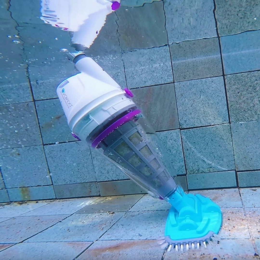 Underwater action photo of the full white, purple, and blue Kokido Telsa 50 cordless handheld pool vacuum operating along the tiled wall and floor of a swimming pool.