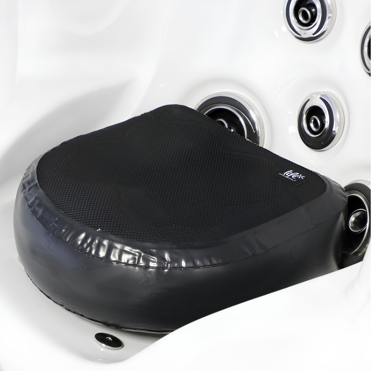 A black Life Spa Booster Seat cushion placed inside a white acrylic hot tub corner seat, illustrating how the elevated water-filled cushion fits securely next to chrome hydrotherapy massage jets.