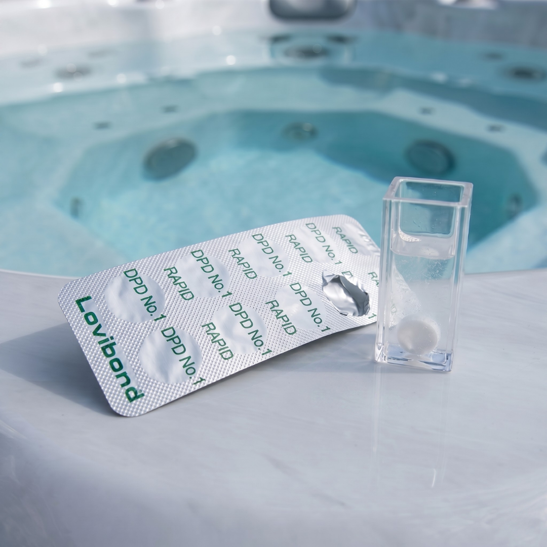 A 10-pack strip of Lovibond DPD No. 1 Rapid tablets next to a square test vial containing a white tablet, sitting on the edge of an outdoor spa for free chlorine testing.