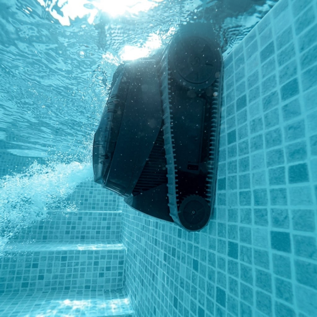 Underwater action shot looking up at the Maytronics Dolphin Liberty 200 robotic pool cleaner as it climbs vertical mosaic pool tiles while expelling a stream of water from its rear propulsion jet near the surface.