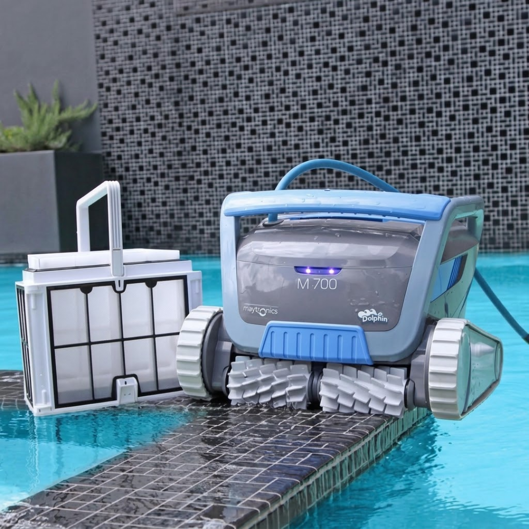 Poolside lifestyle view of the dark grey Maytronics Dolphin M 700 robotic pool cleaner resting on tiled pool coping next to its removed ultra-fine filter basket.