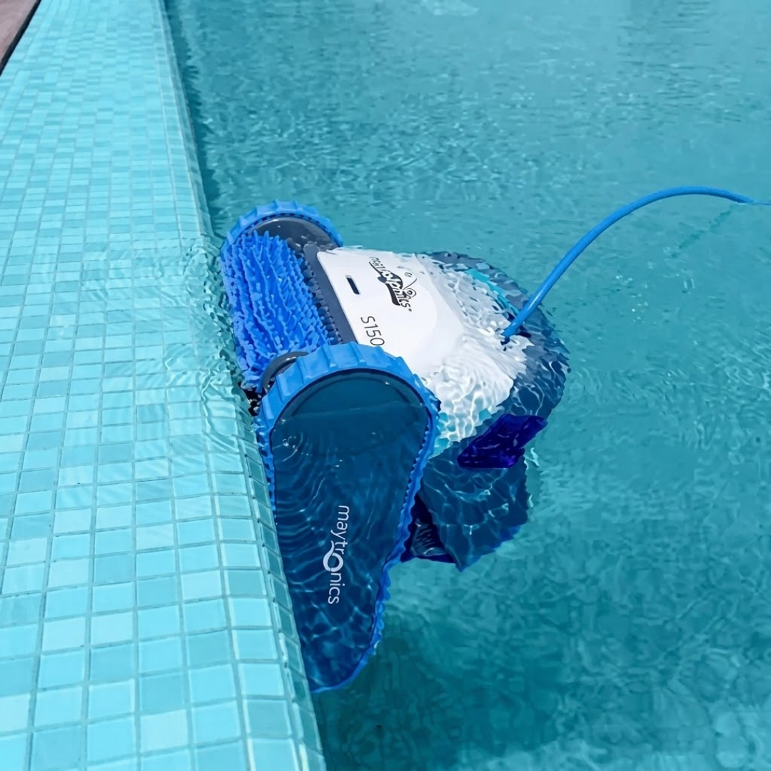 Lifestyle image of the Maytronics Dolphin S 150 robotic pool cleaner operating at the surface, using its active front brush to scrub along the tiled pool waterline.