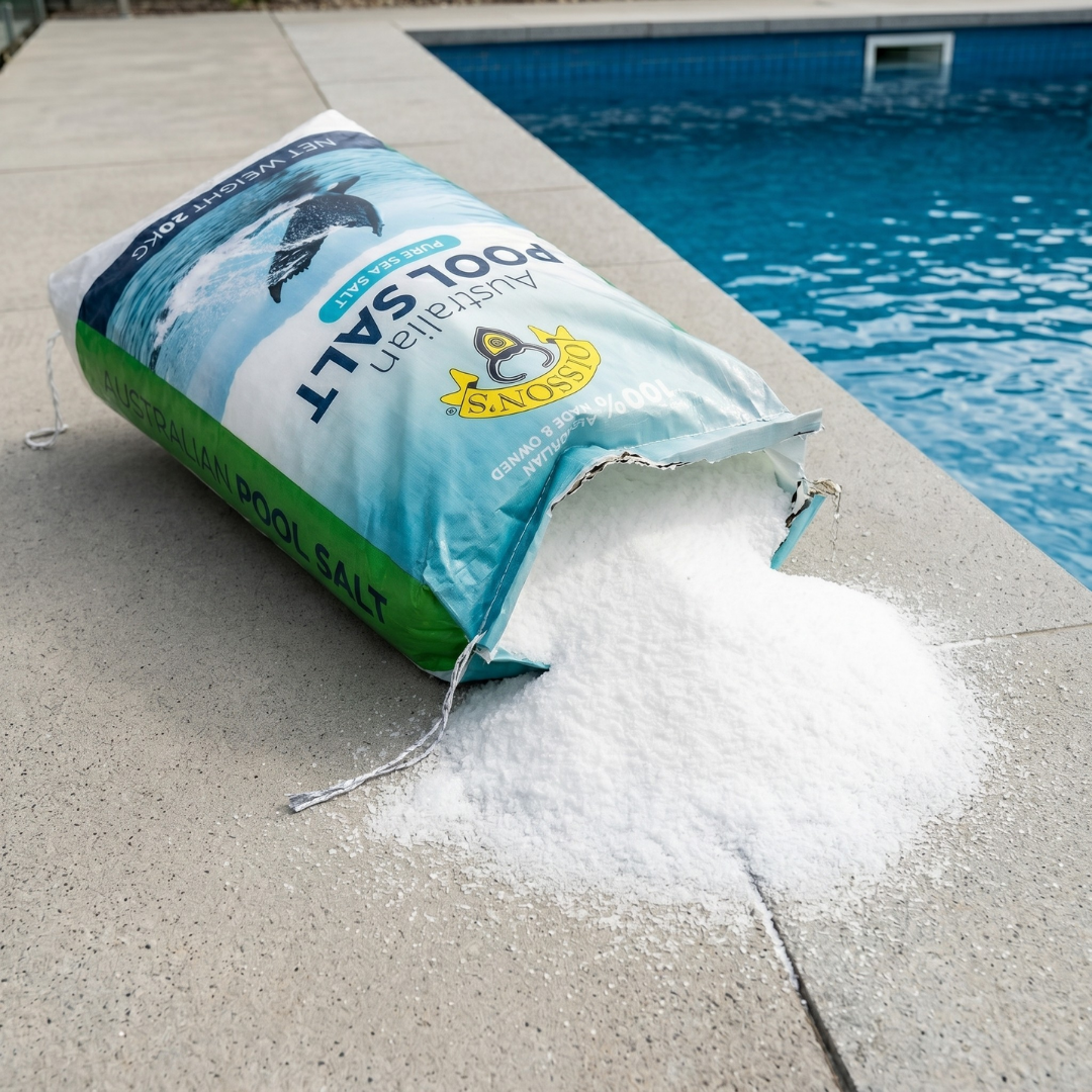 An open 20kg bag of Olsson's Australian Pool Salt poured onto a concrete patio next to a swimming pool, showing the fine white texture of the pure sea salt crystals.