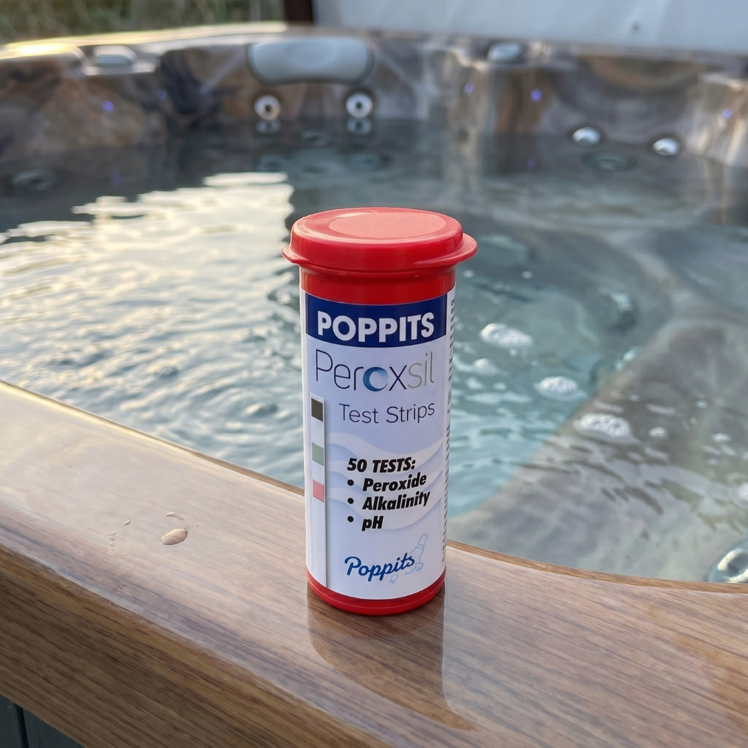 A bottle of Poppits Peroxsil Test Strips sitting on the acrylic edge of an outdoor spa, used for monitoring hydrogen peroxide, alkalinity, and pH levels in chlorine-free hot tubs.