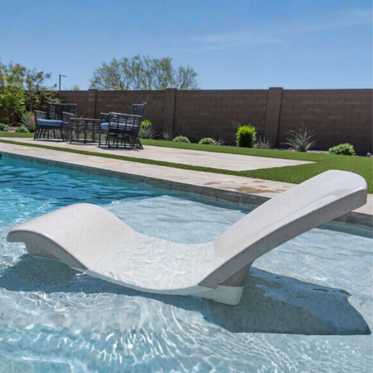 An empty S.R. Smith Destination Series in-pool rocking lounge chair in Seashell finish partially submerged on a shallow pool tanning ledge.