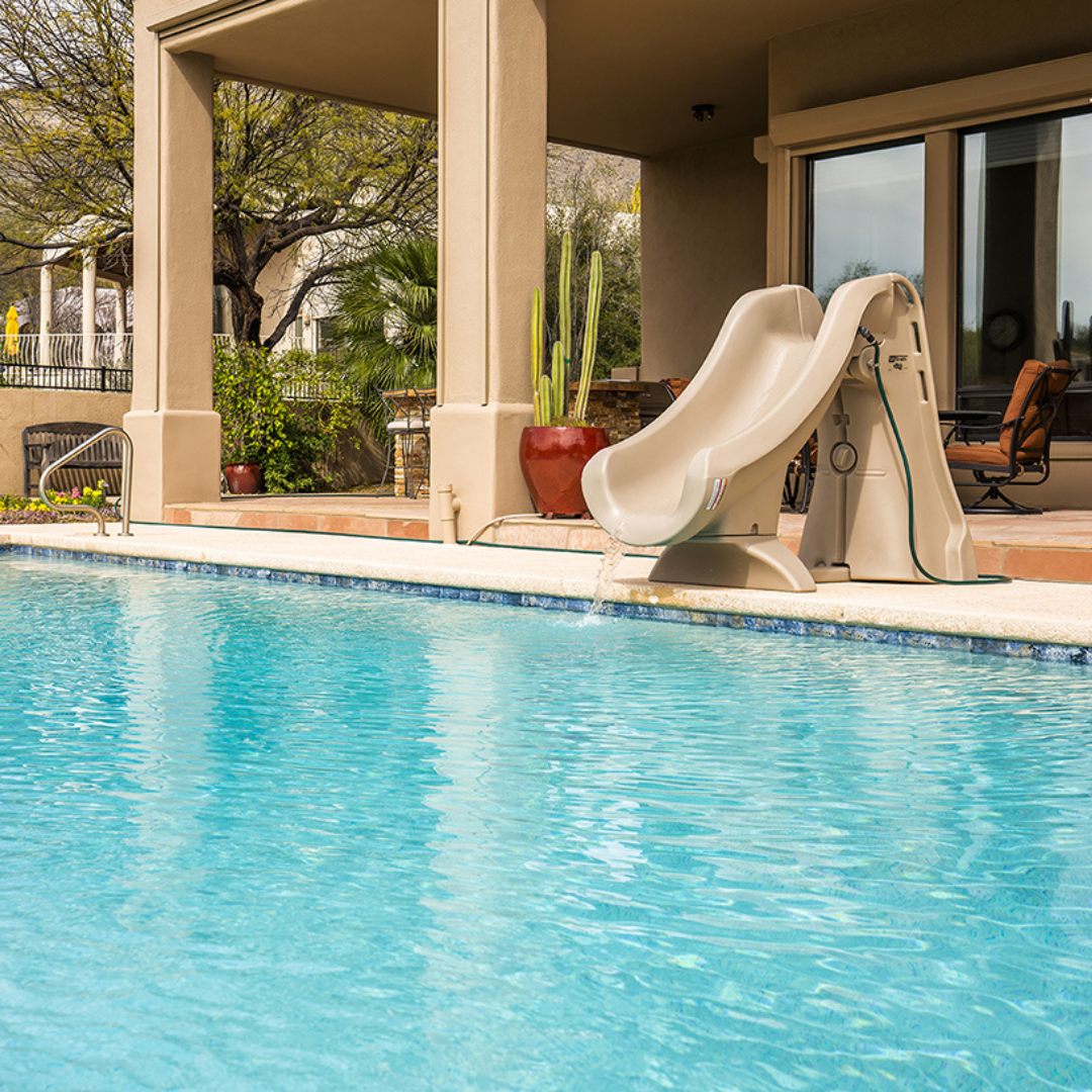 S.R.Smith SlideAway taupe removable water slide installed on a concrete patio deck next to a residential inground swimming pool.