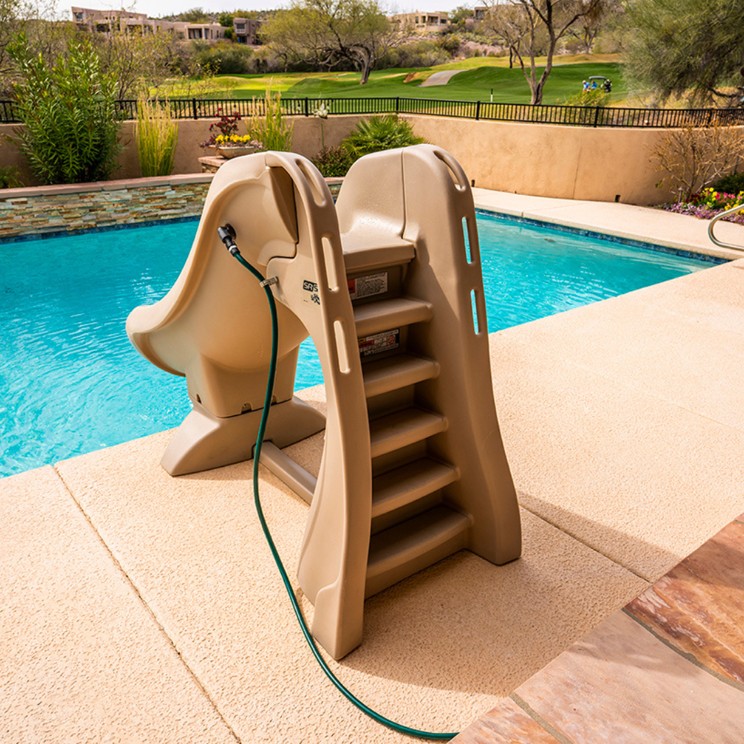 An adult using a rolling dolly cart to transport a compact taupe S.R.Smith SlideAway removable pool slide across a concrete backyard patio patio.