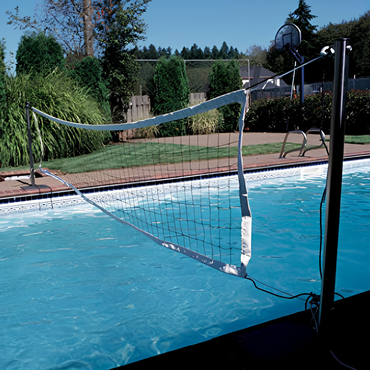S.R. Smith Swim N' Spike volleyball net game installed across a backyard inground swimming pool with a pool basketball hoop in the background.