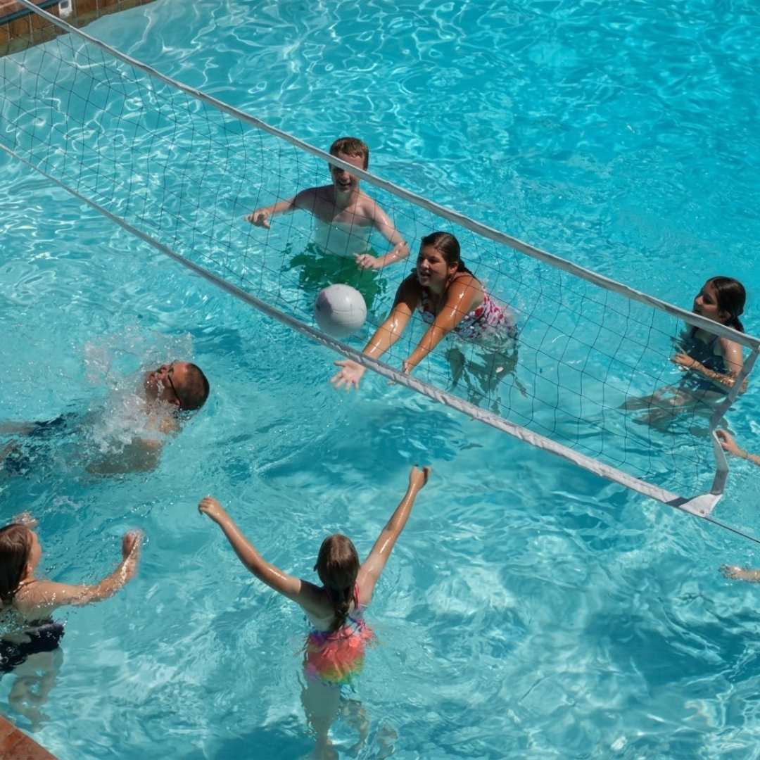 High-angle outdoor lifestyle photo of a family playing water volleyball in a swimming pool with an S.R. Smith Swim N' Spike pool net system across the clear blue water.