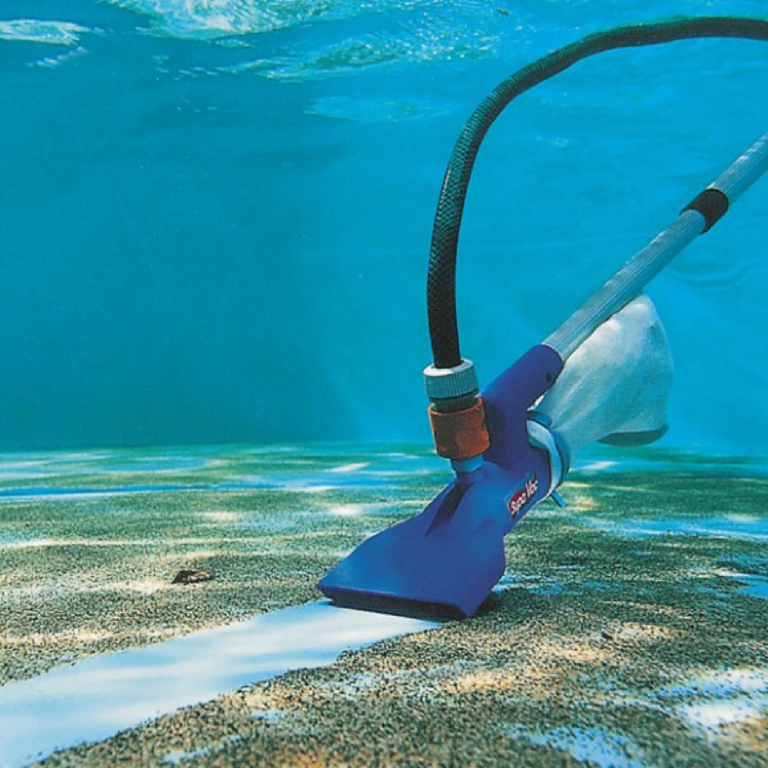Underwater view of a blue Swimsafe Supa-Vac pool cleaner vacuuming a thick layer of dirt and debris from the bottom of a swimming pool, leaving a clean white path behind it.