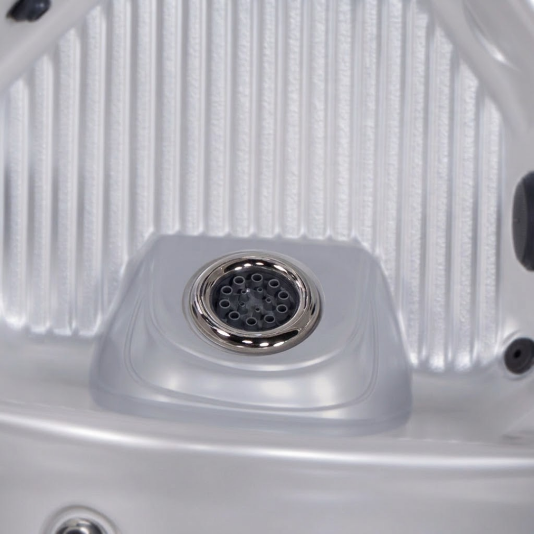 Close-up view of a single Ultra Blaster 7 SS Graphite spa jet installed in the raised footwell dome of a silver acrylic hot tub shell.