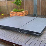 A slate grey three-piece custom spa hard cover installed on a dark timber pool deck in a landscaped backyard.
