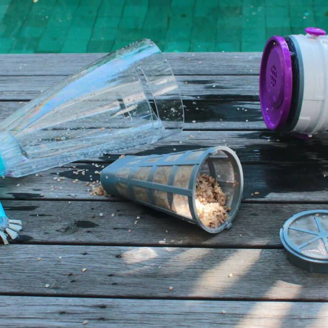 Disassembled Kokido Telsa 50 pool vacuum components on a wooden deck next to a pool, showing the grey mesh filter cone filled with collected sand and debris alongside the clear canister body