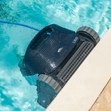Top-down outdoor lifestyle view of the Maytronics Dolphin S3000 robotic pool cleaner scrubbing along the pool waterline, showing its front active brush, dark navy chassis, S3000 branding, continuous tracks, and blue power cable floating in clear blue water.