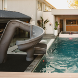 S.R.Smith Helix2 grey spiral water slide with active water spray nozzles installed next to a luxury residential inground swimming pool and outdoor cabana.