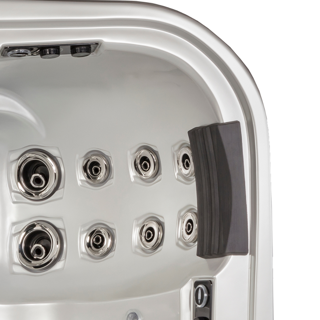 Overhead view of an empty silver acrylic hot tub shell featuring a textured dark grey Artesian Elite lounge headrest pillow and multi-sized stainless steel hydrotherapy massage jets.