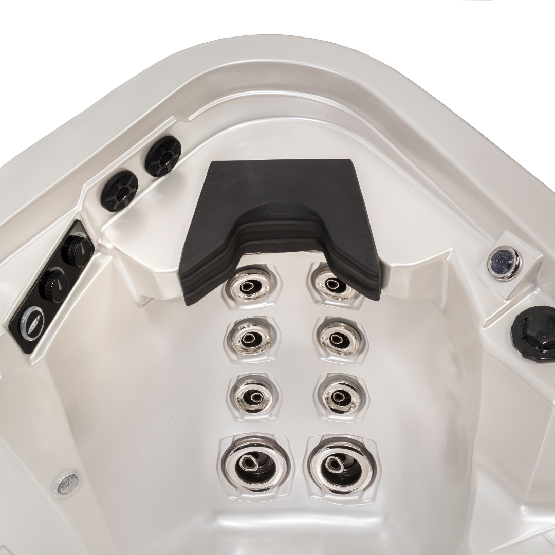 Top-down view of a charcoal black Artesian Elite neck headrest pillow installed in an empty silver pearl acrylic hot tub corner seat, situated above an array of multi-level chrome hydrotherapy back jets.