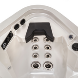 Top-down view of a charcoal black Artesian Elite neck headrest pillow installed in an empty silver pearl acrylic hot tub corner seat, situated above an array of multi-level chrome hydrotherapy back jets.