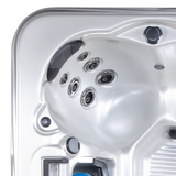 High-angle view of an Artesian Spas Island Lounge charcoal grey headrest pillow mounted inside a contoured silver hot tub shell featuring a multi-jet hydrotherapy cluster.