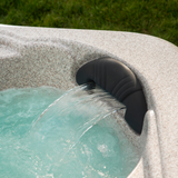 An Artesian Spas Island series charcoal grey waterfall headrest pillow installed in a textured granite look hot tub shell, with water flowing through its bottom cut-out arch.