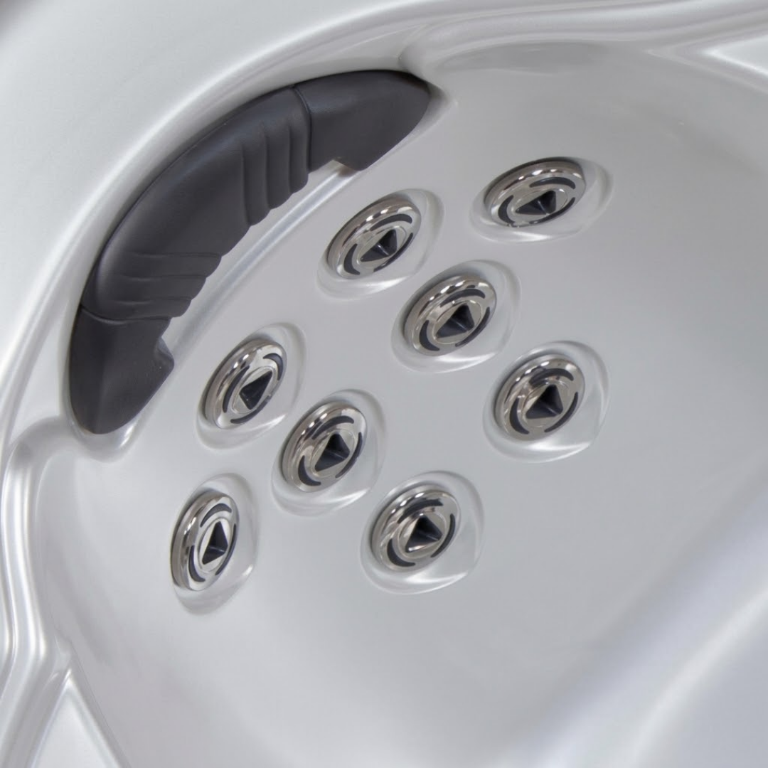 Angled view of multiple Artesian C-Helix 2.75 SS spa jets installed in an array below a padded headrest within a white acrylic hot tub shell.
