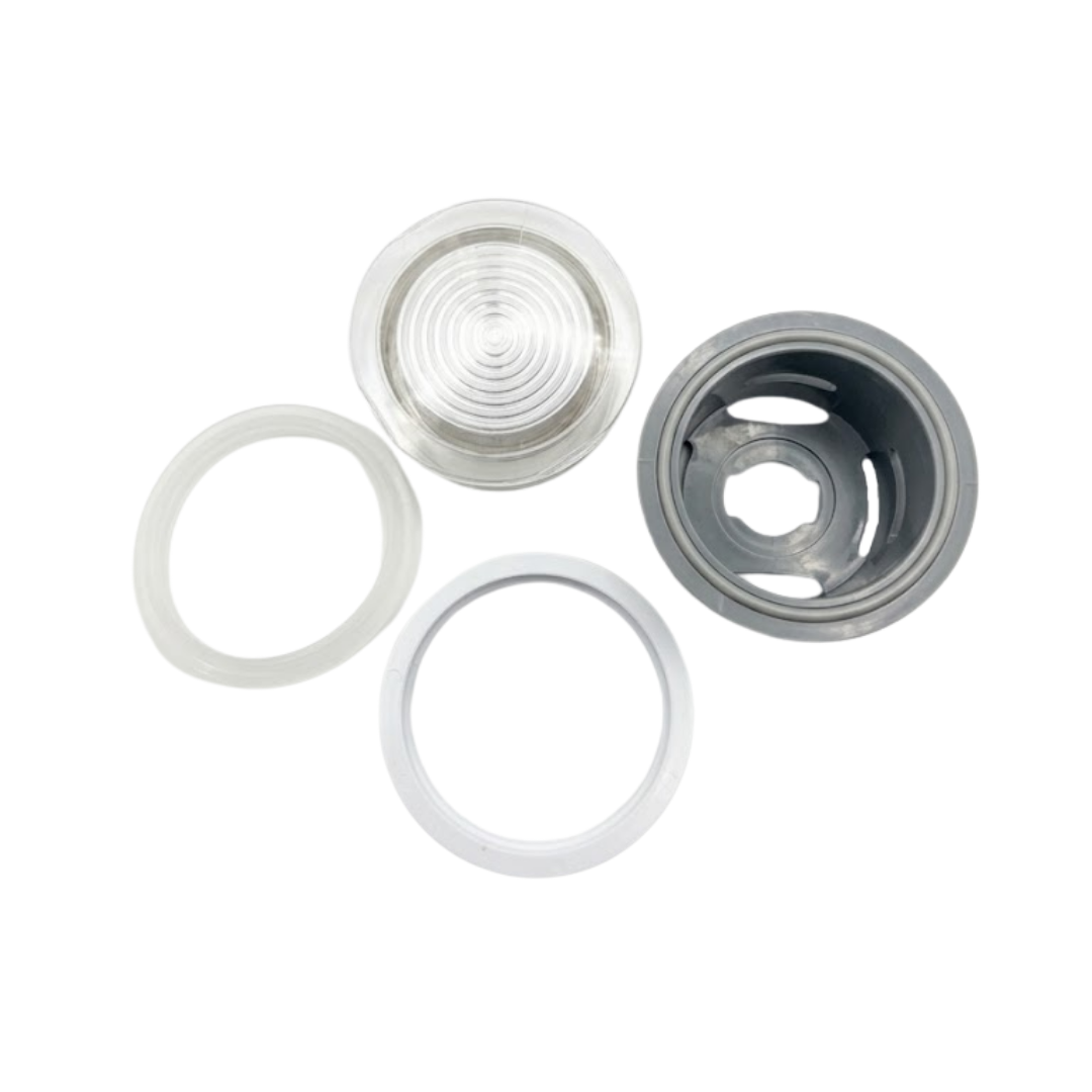 Exploded view of the Artesian 2-inch Xylex/PVC light lens assembly, showing the clear ribbed front lens, translucent sealing gasket, white mounting ring, and grey rear socket housing isolated on white.