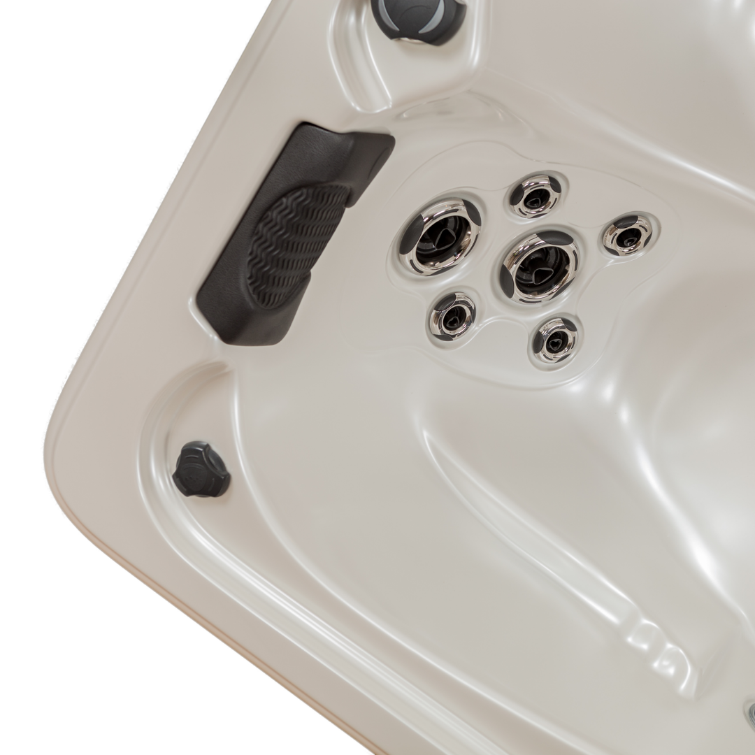 Top-down angle view of a dark charcoal black foam lounger headrest pillow installed in an empty cream acrylic hot tub seat, situated directly above a cluster of adjustable chrome massage jets.