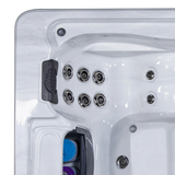 Overhead top-down view of a dark charcoal black foam lounger headrest pillow installed in an empty white acrylic hot tub corner seat, located next to a group of chrome hydrotherapy jets and a blue and purple spa filter bay.