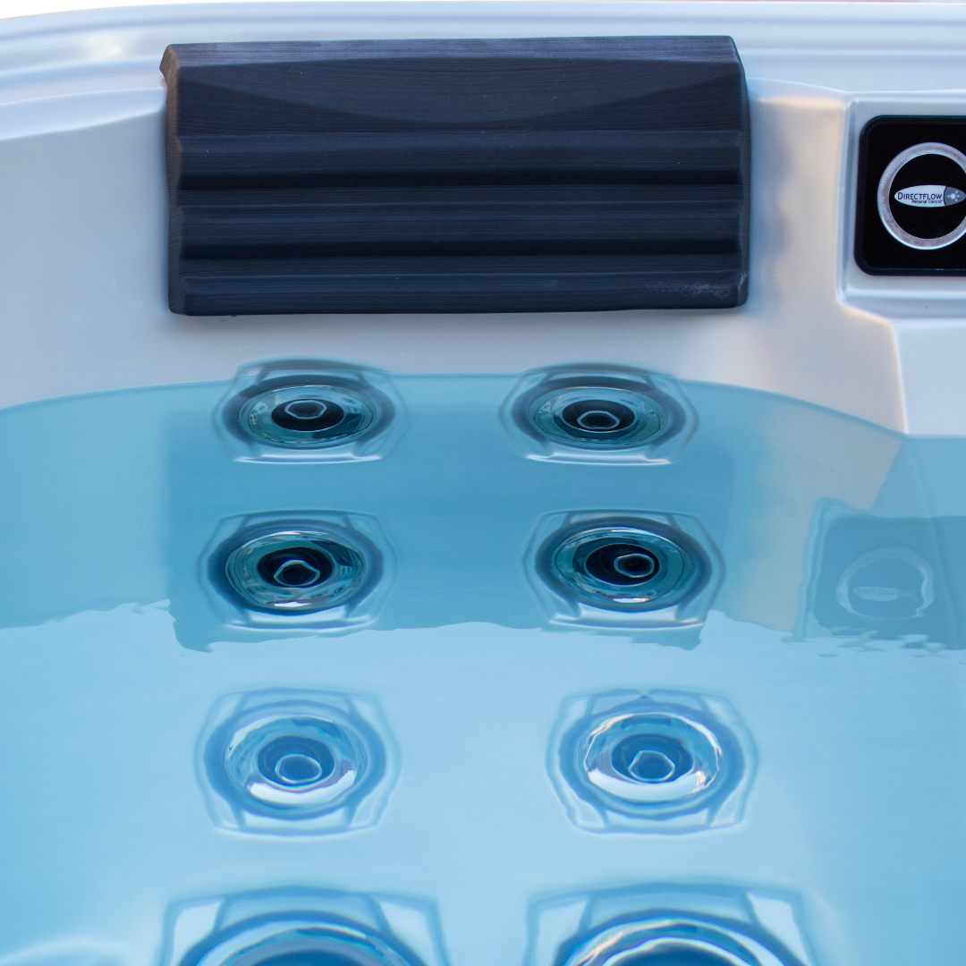 Direct view of a charcoal black textured Artesian Elite lounge headrest pillow mounted above a matrix of hydrotherapy spa jets submerged in clear blue water.