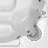 Overhead view of a curved silver grey foam neck headrest pillow without a logo, installed in a white acrylic hot tub corner seat near water jets and air dials.