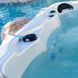 A wide angle lifestyle view of a black 2 inch Artesian Spas diverter valve handle knob installed on the white acrylic deck rim of a hot tub next to running water pointed out by a blue arrow