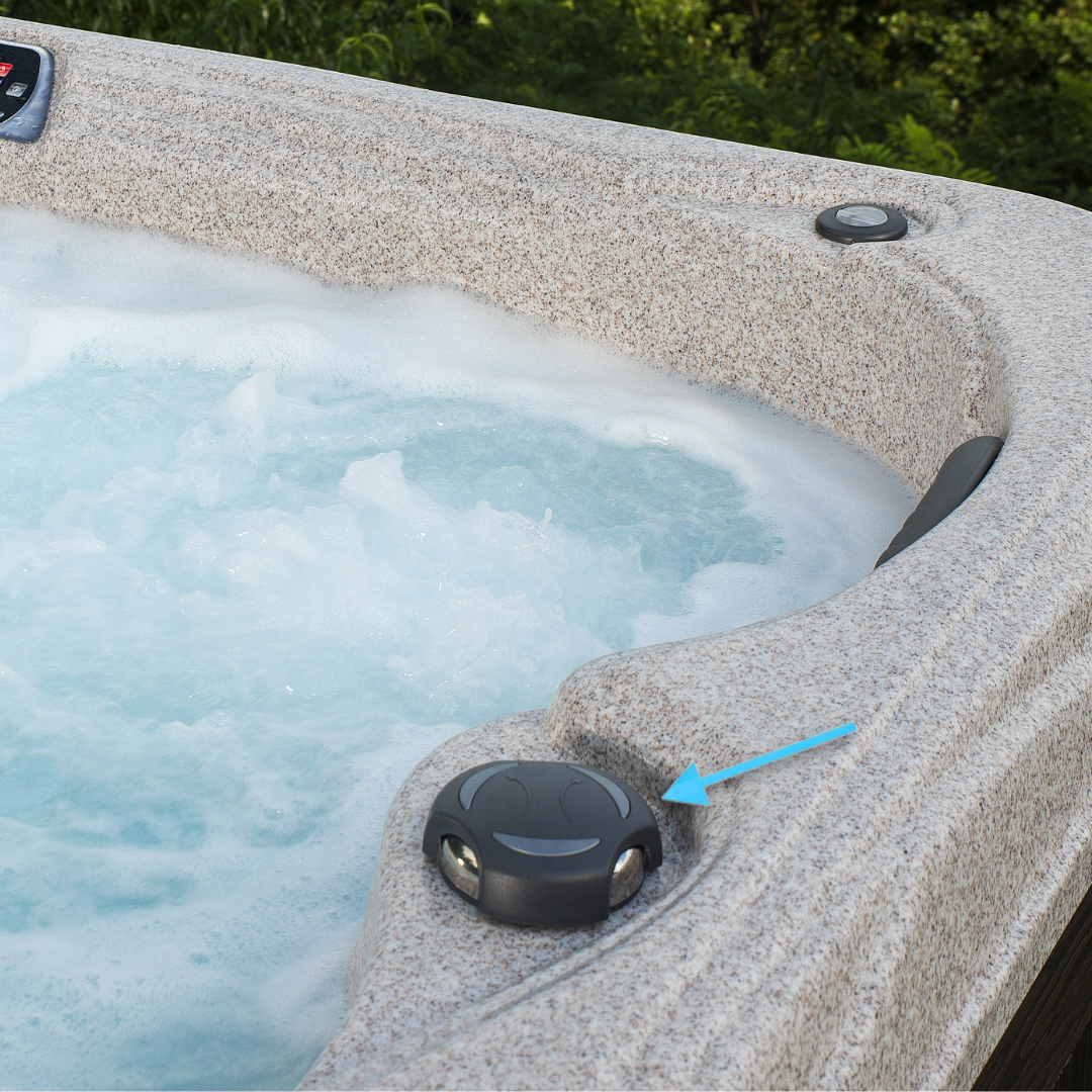 A wide angle outdoor view of a black 2 inch Artesian Spas diverter valve handle knob installed on a textured grey speckled faux stone hot tub pointed out by a blue arrow