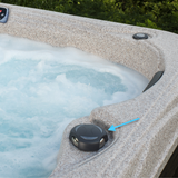 A wide angle outdoor view of a black 2 inch Artesian Spas diverter valve handle knob installed on a textured grey speckled faux stone hot tub pointed out by a blue arrow