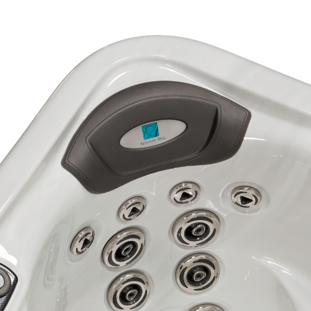 Top-down angle view of a grey curved replacement foam headrest pillow with its central silver logo dome installed in a white acrylic hot tub corner seat, located above a cluster of chrome massage jets.