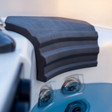 Close-up side perspective of a charcoal black curved Elite corner headrest pillow installed in a filled hot tub, highlighting its stacked ridge texture and position directly above the waterline and chrome jets.