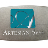 Macro close-up shot of a metallic silver replacement resin dome label for an Artesian Spas hot tub headrest pillow, focusing on the stylized teal square "A" logo and engraved style "ARTESIAN SPAS" branding text.